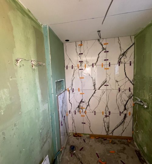 Pose du carrelage effet marbre – douche italienne Étanchéité, niche intégrée et habillage mural en cours.